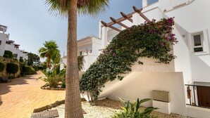 A white building with a pergola covered in flowering vines, palm trees, and a paved pathway. - RDR230 - Apt. Aloha Royal (Marbella)