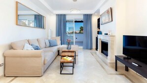 A modern living room with a beige sofa, a coffee table, a TV, and a fireplace. - RDR230 - Apt. Aloha Royal (Marbella)