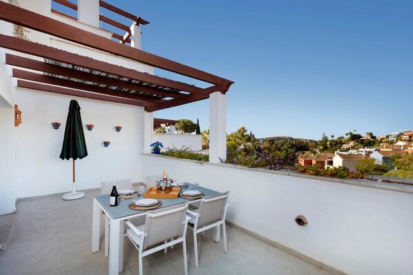 A rooftop terrace with a table set for two, a pergola, and a view of the city. - RDR230 - Apt. Aloha Royal (Marbella)