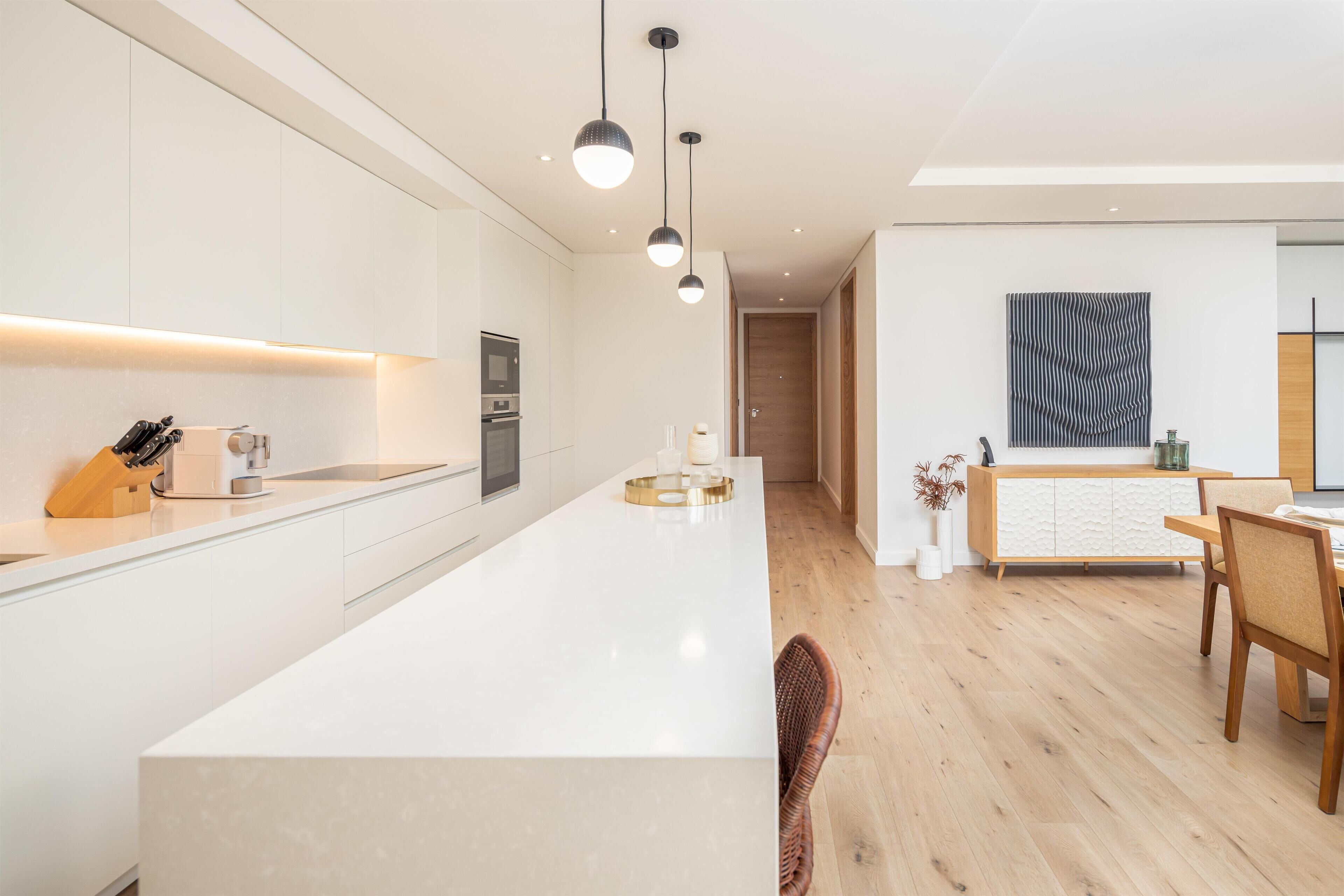 Een moderne keuken met een centraal eiland, hangende lampen en een eethoek met een houten tafel en stoelen.