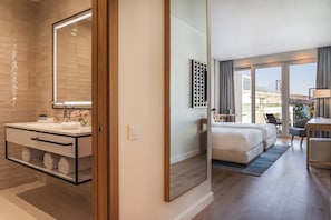 A modern hotel room with a large mirror, a bathroom with a vanity, a bed, a desk, and a view of a bridge.