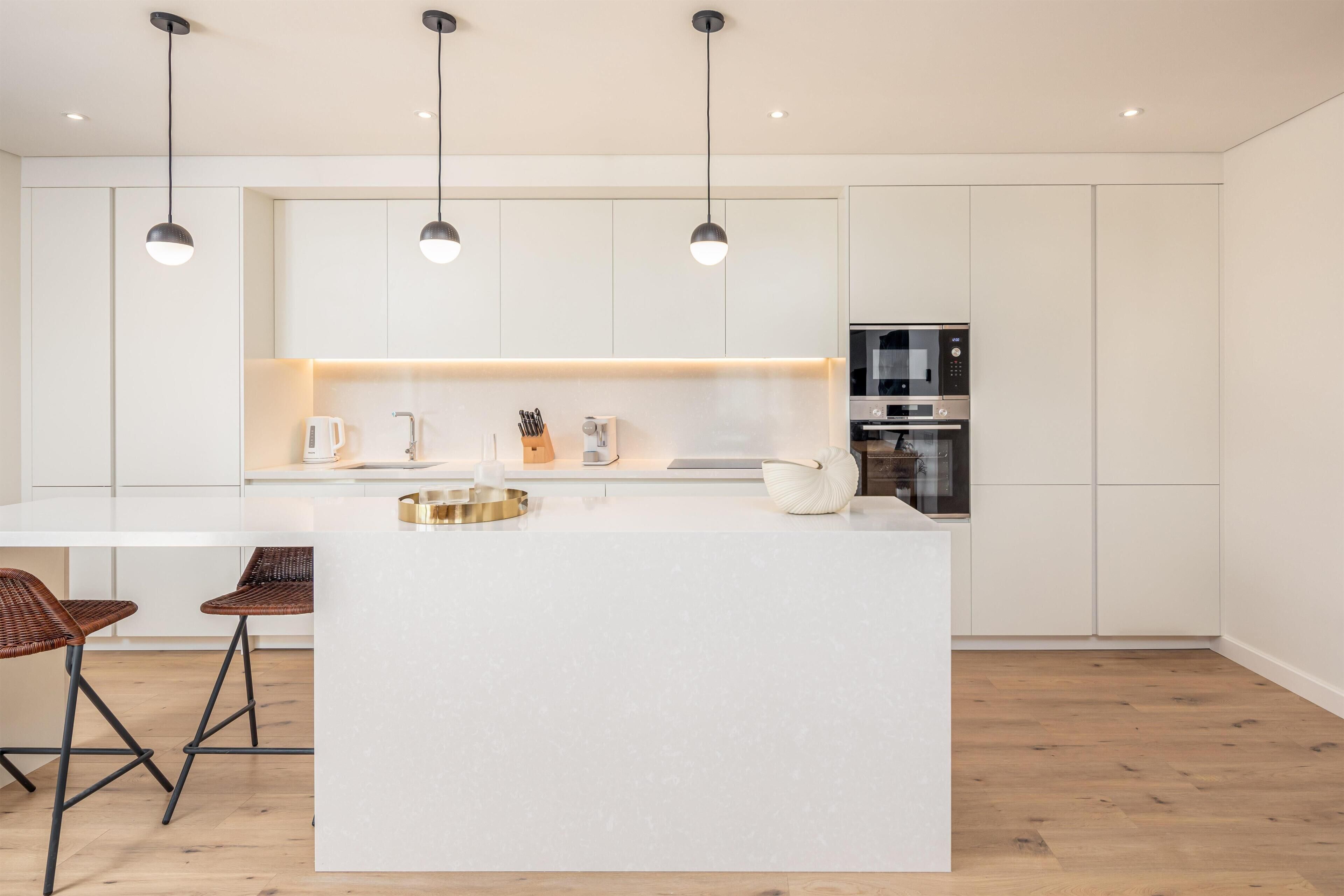 Una cocina moderna con armarios blancos, una isla central, iluminación colgante y un horno empotrado.