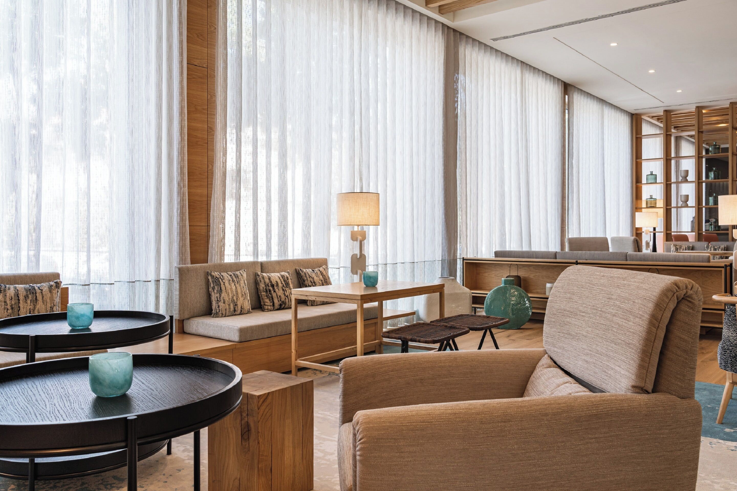 A modern hotel lobby with a sofa, two round tables, a lamp, and a bookshelf.
