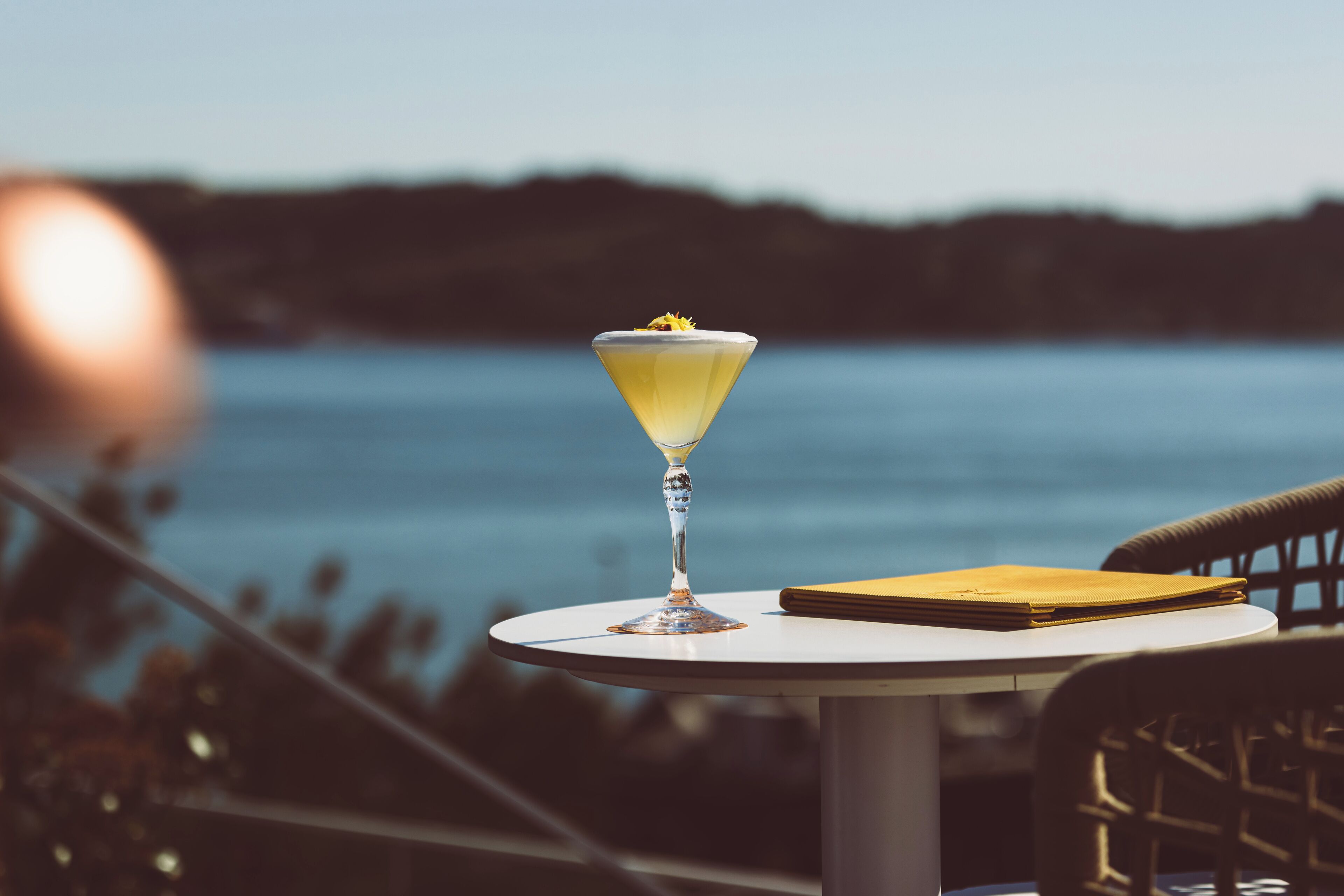 Un bicchiere da martini con una guarnizione gialla su un tavolo bianco, vicino all'acqua.