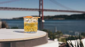 A glass of drink on a table with a view of a bridge in the background.