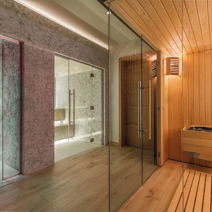 A modern spa room with a glass shower enclosure, wooden flooring, and a wooden sauna area.