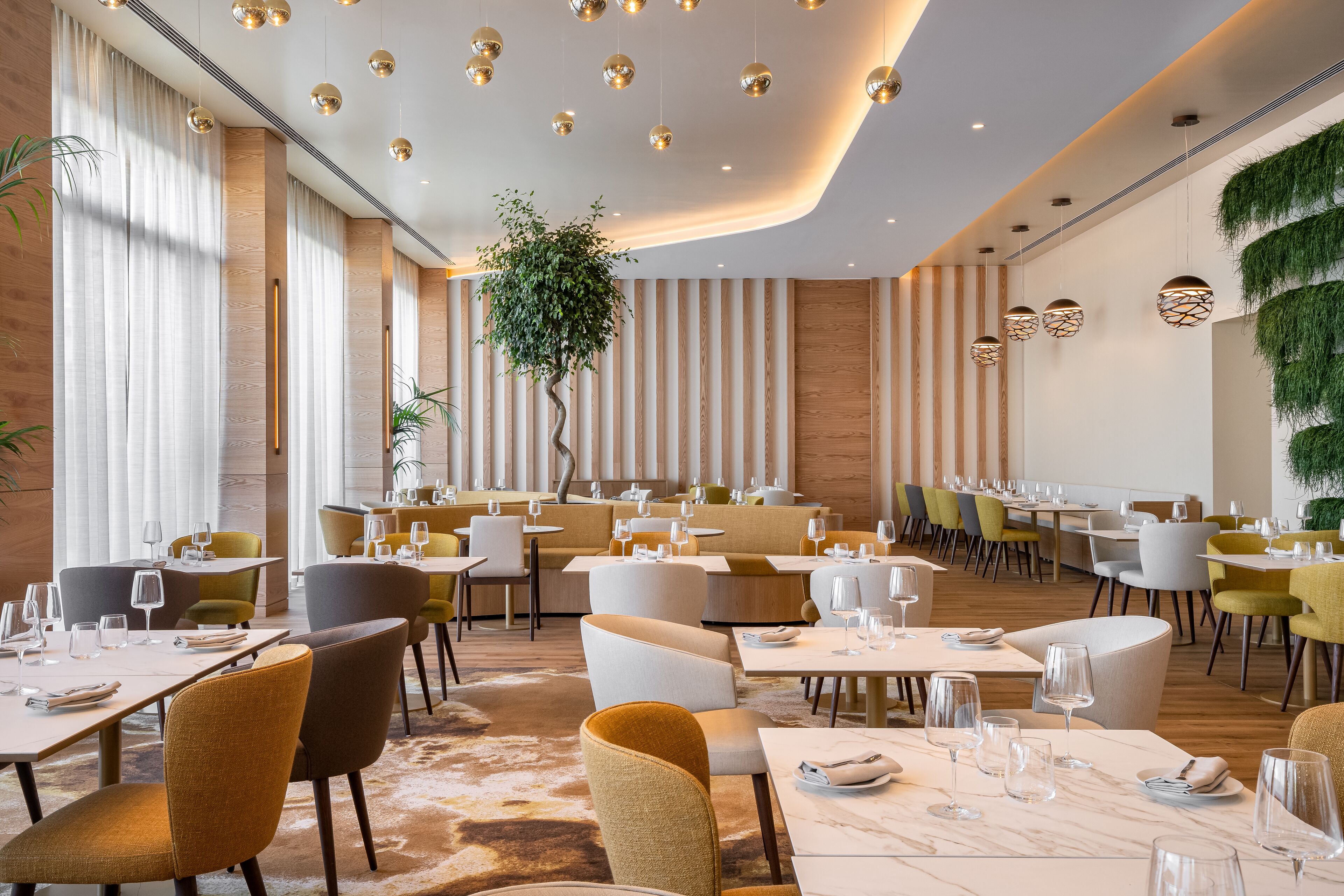 A modern restaurant with round tables, chairs, and hanging spherical lights.