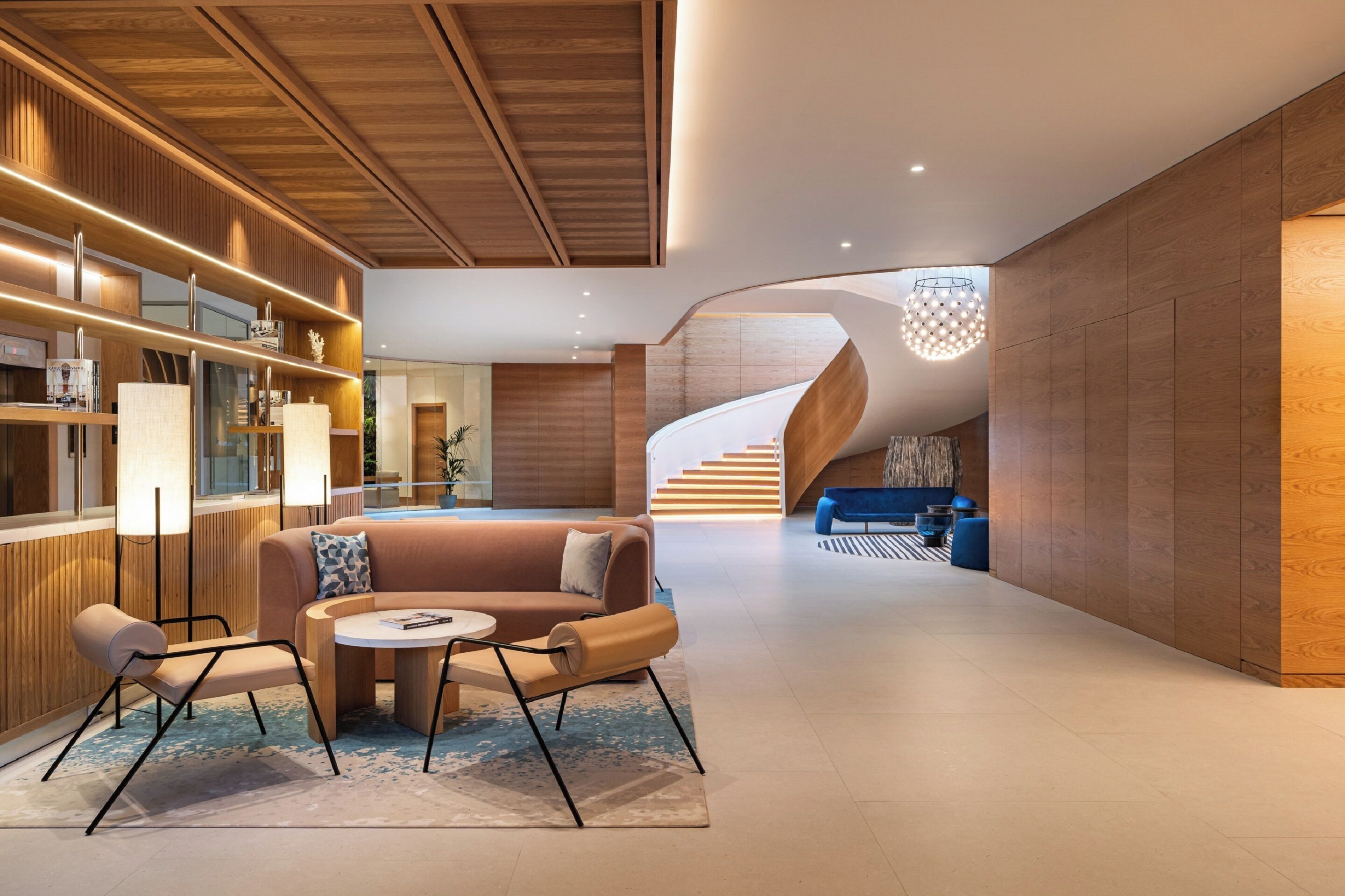 Un intérieur moderne avec un escalier en colimaçon, un coin salon doté d’une table ronde et un mur revêtu de panneaux en bois.