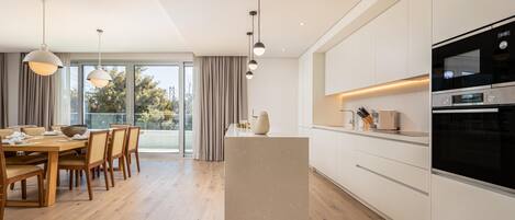 Et moderne køkken med en central ø, integrerede hårde hvidevarer og et spiseområde med naturligt lys.