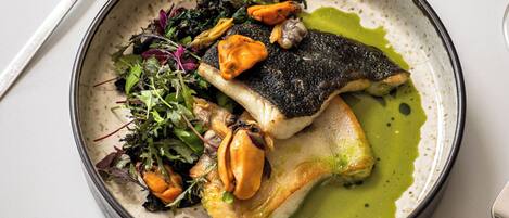 A plate of food with a fish, greens, and a green sauce.