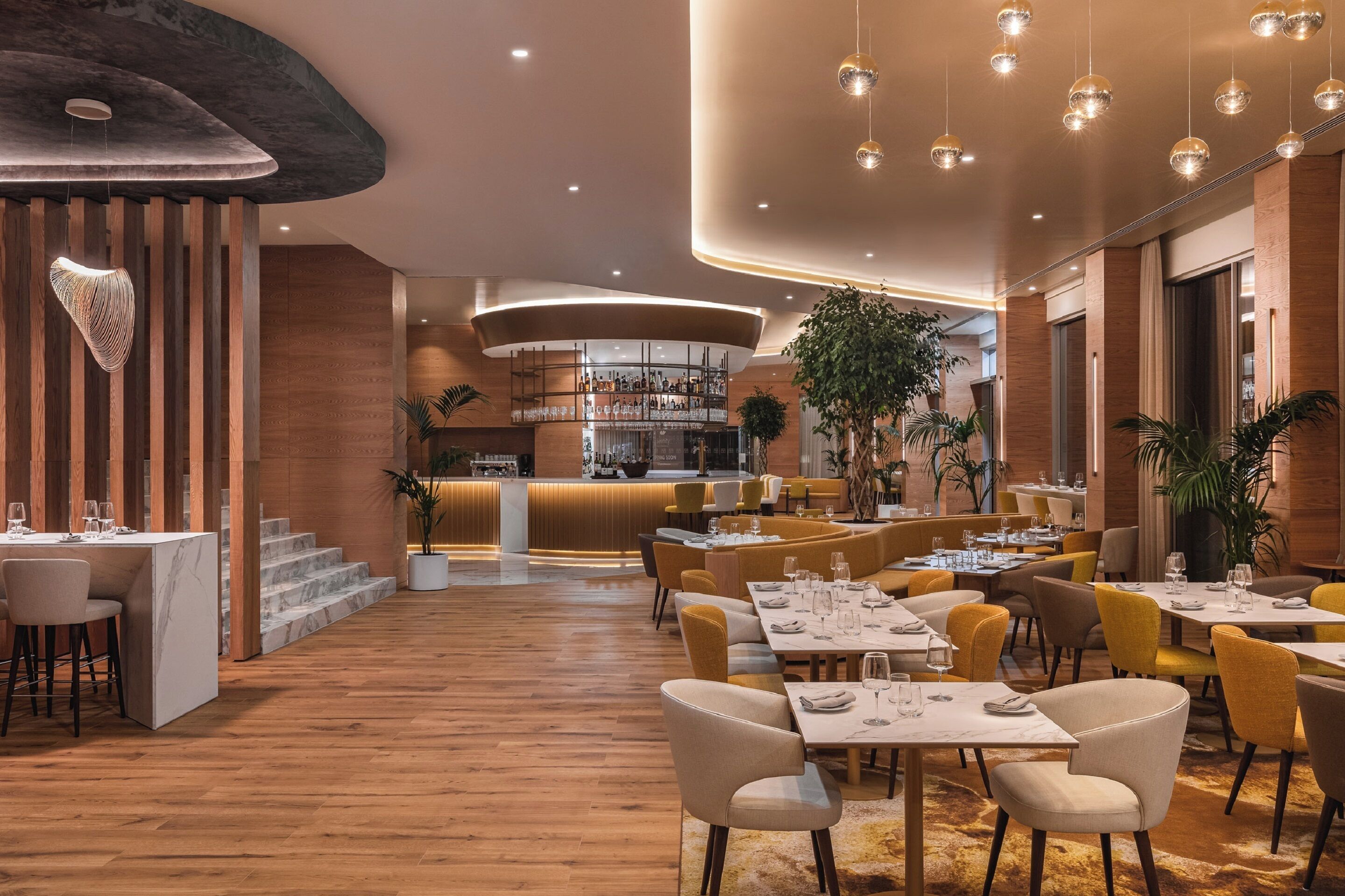 A modern restaurant with wooden floors, a bar area, and yellow chairs.