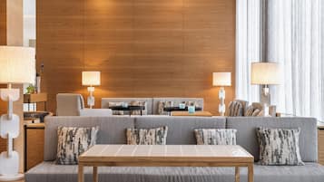 A modern hotel lobby with a grey sofa set, a wooden coffee table, and two lamps.