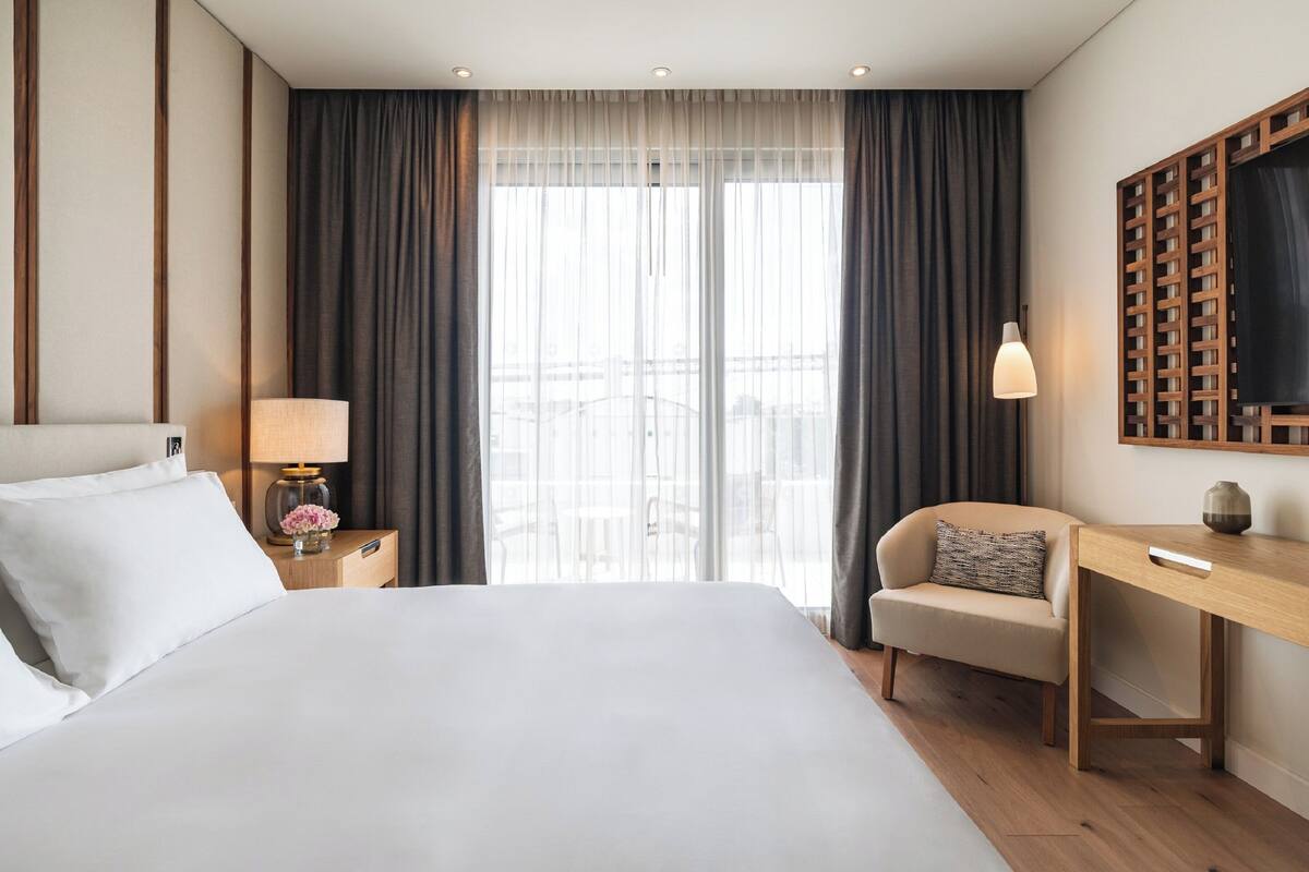 A hotel room with a large bed, a desk, a chair, a lamp, and a TV on a wooden stand.