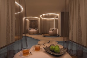 A modern room with a round table, two chairs, a bowl of green apples, and a cup of tea.