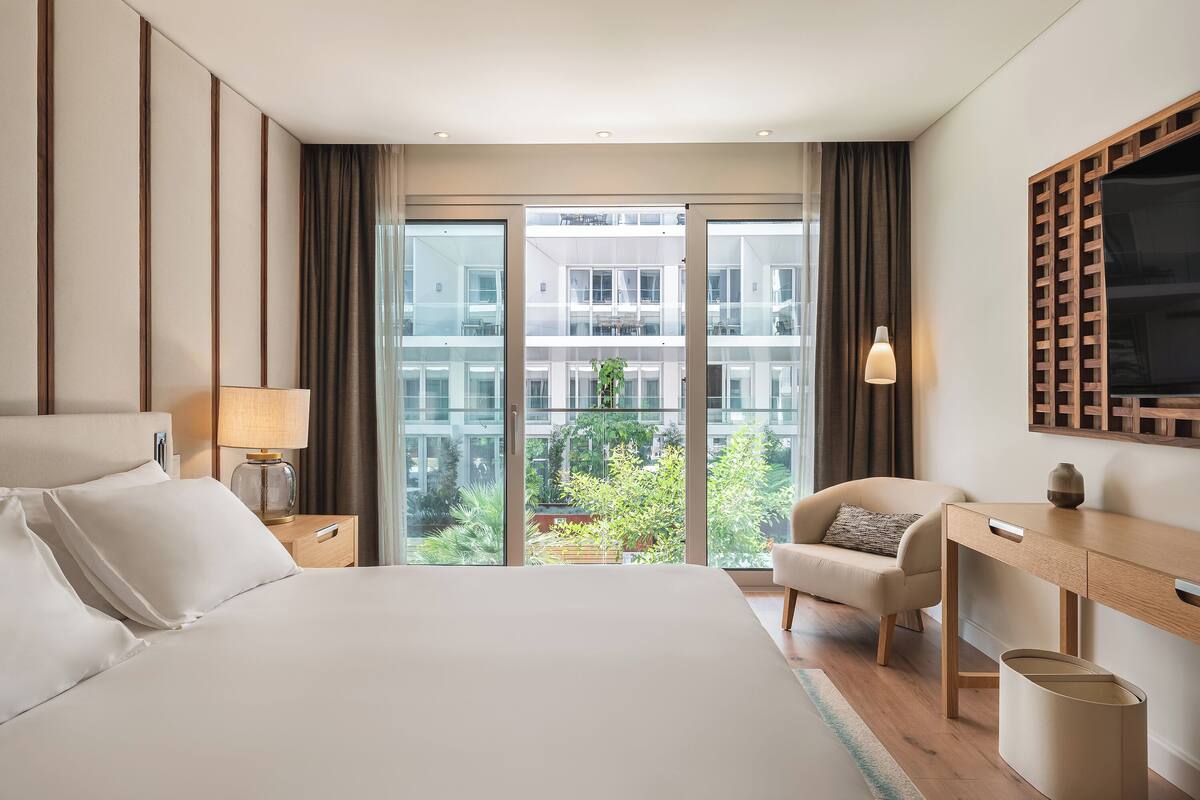 A hotel room with a large bed, a desk, a chair, a lamp, and a TV.