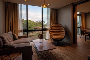 A modern living room with a sofa, a unique egg-shaped chair, a coffee table, and a view of the outdoors through large windows. - SALT of Akagera (Mwiri)