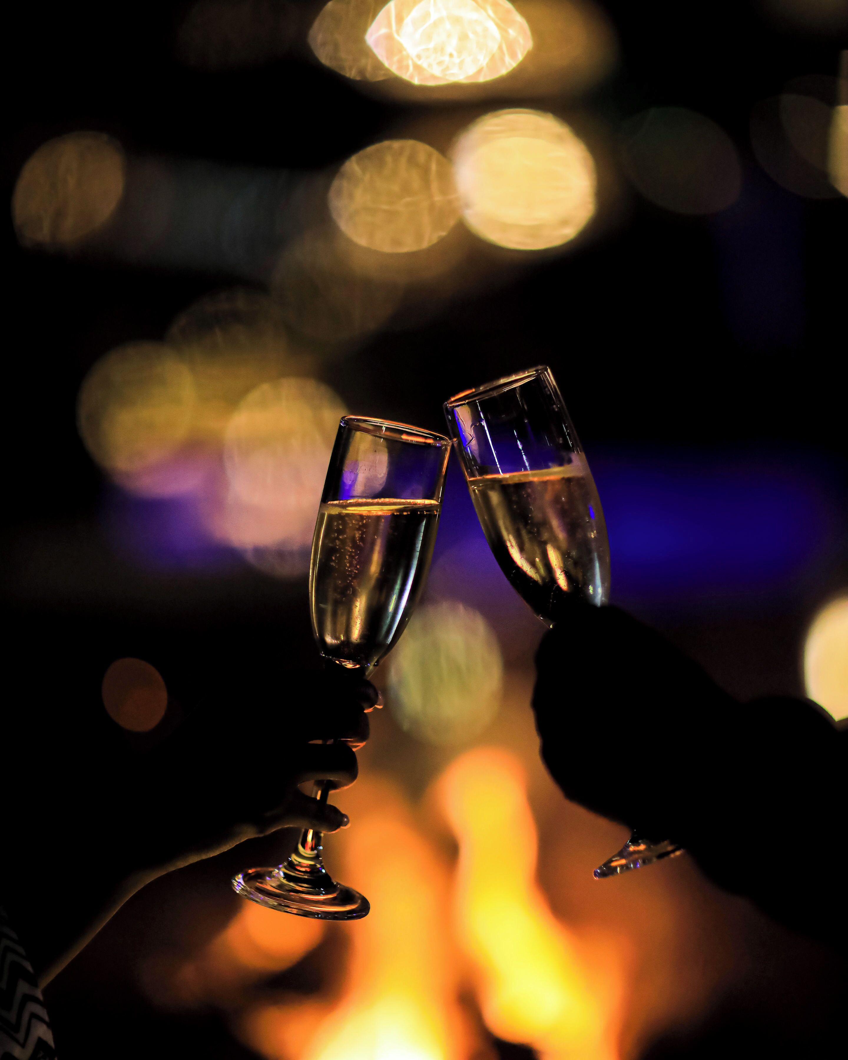 Zwei Gläser einer klaren Flüssigkeit, möglicherweise Champagner, werden von Händen vor unscharfem Hintergrund mit Bokeh-Lichtern gehalten.