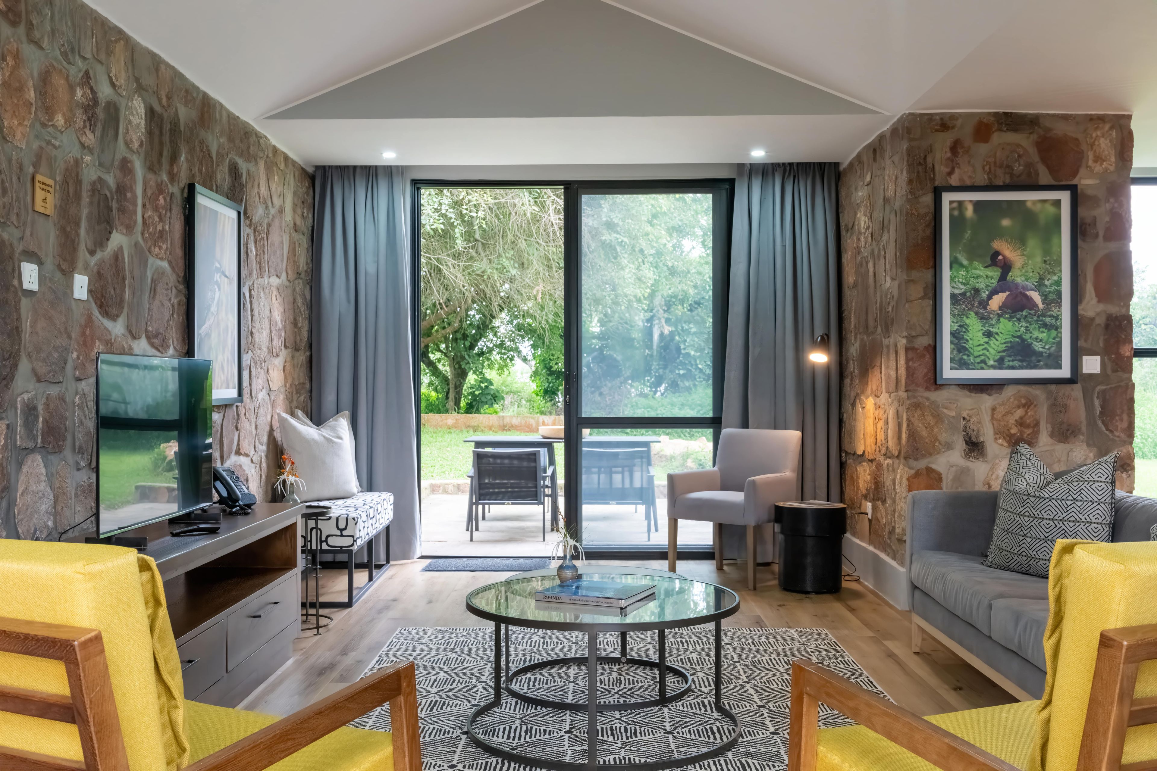 A modern living room with stone walls, a glass coffee table, and a view of the outdoors.