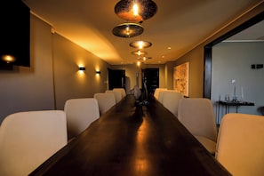 A conference room with a long wooden table and white chairs, a modern ceiling light fixture, and a painting on the wall. - SALT of Akagera (Mwiri)