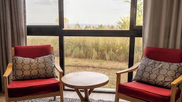 Una habitación con dos sillones tapizados en rojo, una mesa redonda pequeña y un ventanal con vistas al exterior.