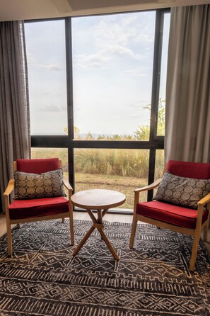 A room with two red upholstered chairs, a small round table, and a large window with a view of the outdoors. - SALT of Akagera (Mwiri)