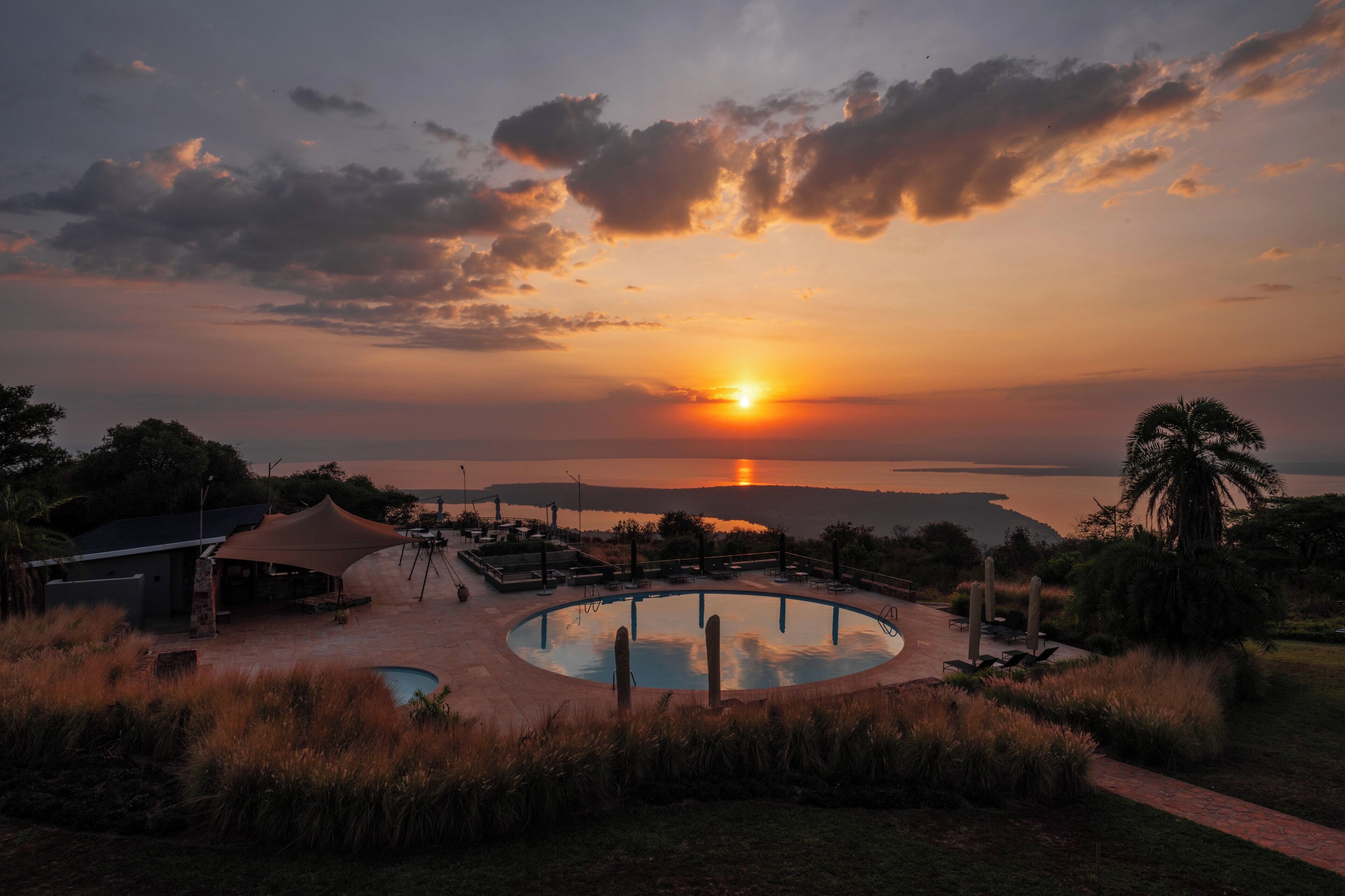 A pool area with a sunset view, surrounded by grass and palm trees.