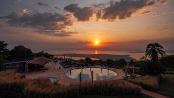 A pool area with a sunset view, surrounded by grass and palm trees.