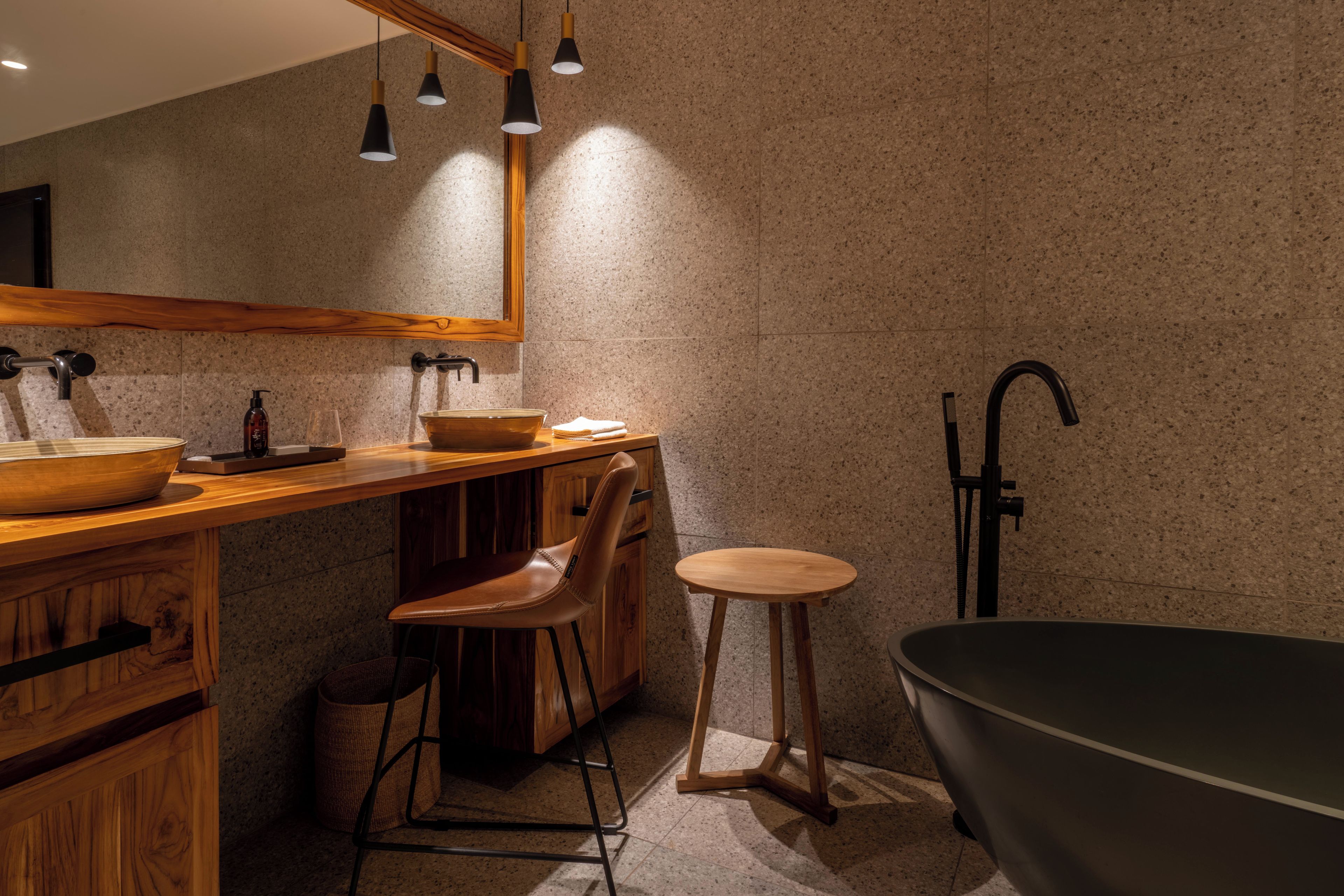 Een moderne badkamer met een houten wastafelmeubel, een losstaand krukje, een ruim vrijstaand bad en een spiegel boven het wastafelmeubel.