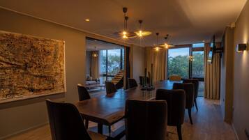 A modern dining area with a large table and chairs, a view of the outdoors through large windows, and a large abstract painting on the wall.