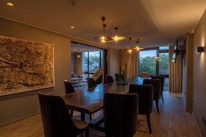A modern dining area with a large table and chairs, a view of the outdoors through large windows, and a large abstract painting on the wall. - SALT of Akagera (Mwiri)