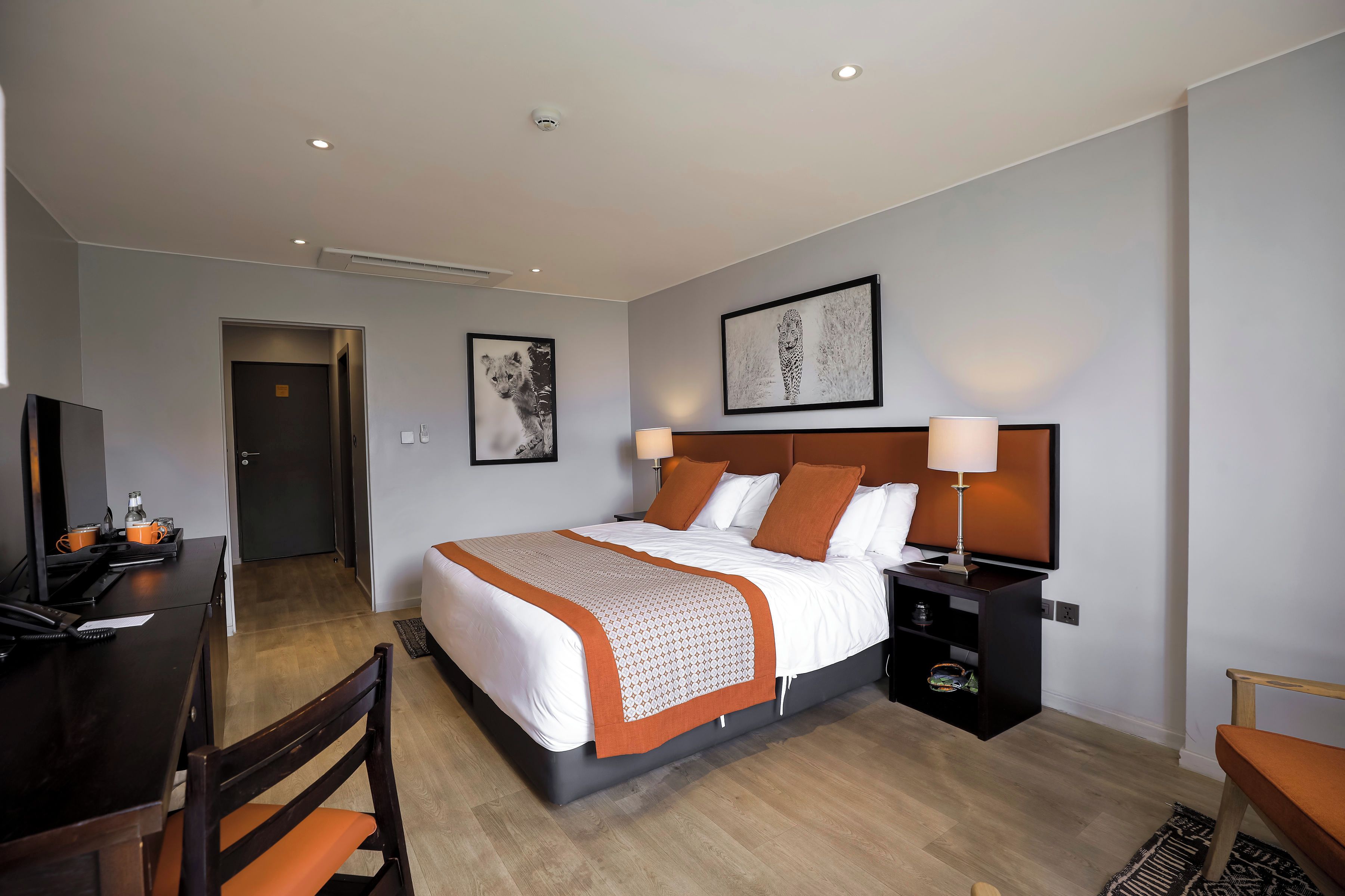 A hotel room with a bed, bedside tables, a desk with a chair, a television, and artwork on the walls.