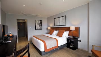 A hotel room with a bed, bedside tables, a desk with a chair, a television, and artwork on the walls.