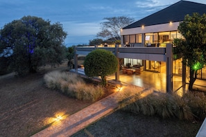 A modern house with a patio area, outdoor seating, and a well-lit entrance. - SALT of Akagera (Mwiri)