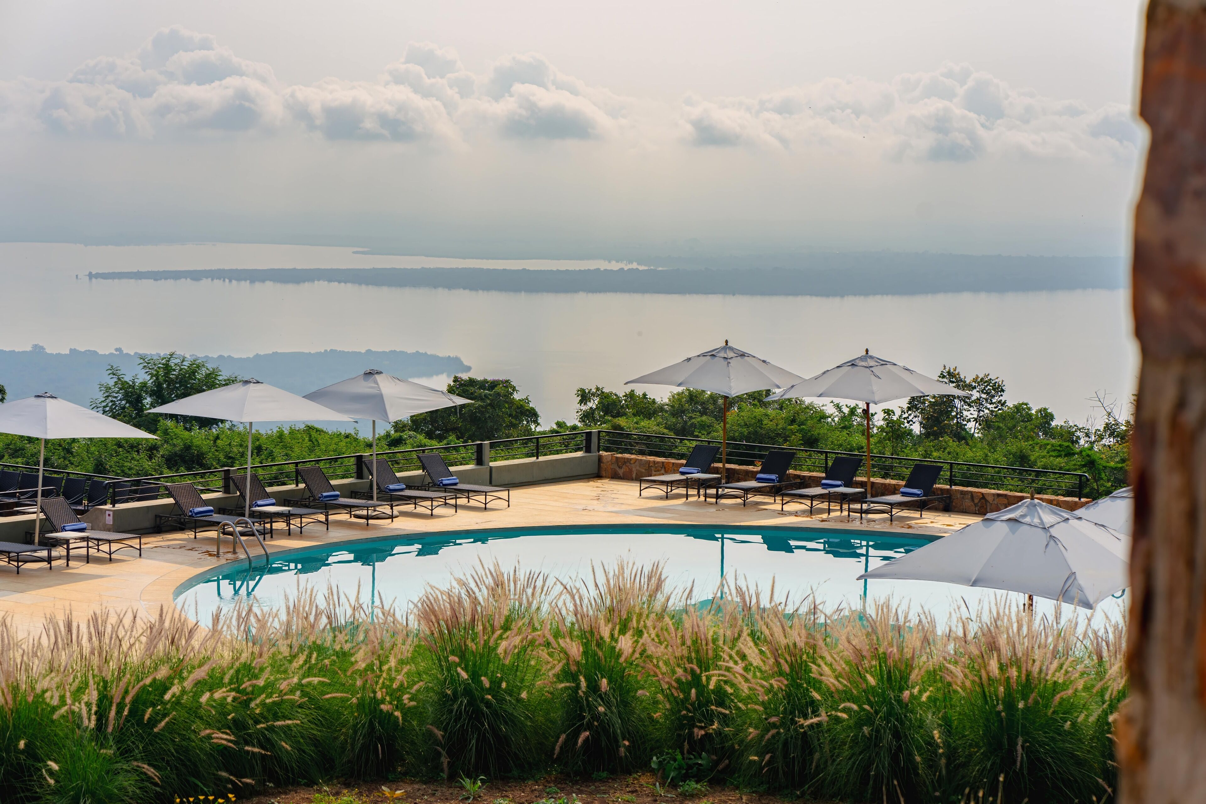 A poolside area with lounge chairs and umbrellas, overlooking a calm body of water and distant land.
