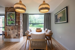 A dining area with a stone accent wall, a large window, and two hanging lamps. - SALT of Akagera (Mwiri)