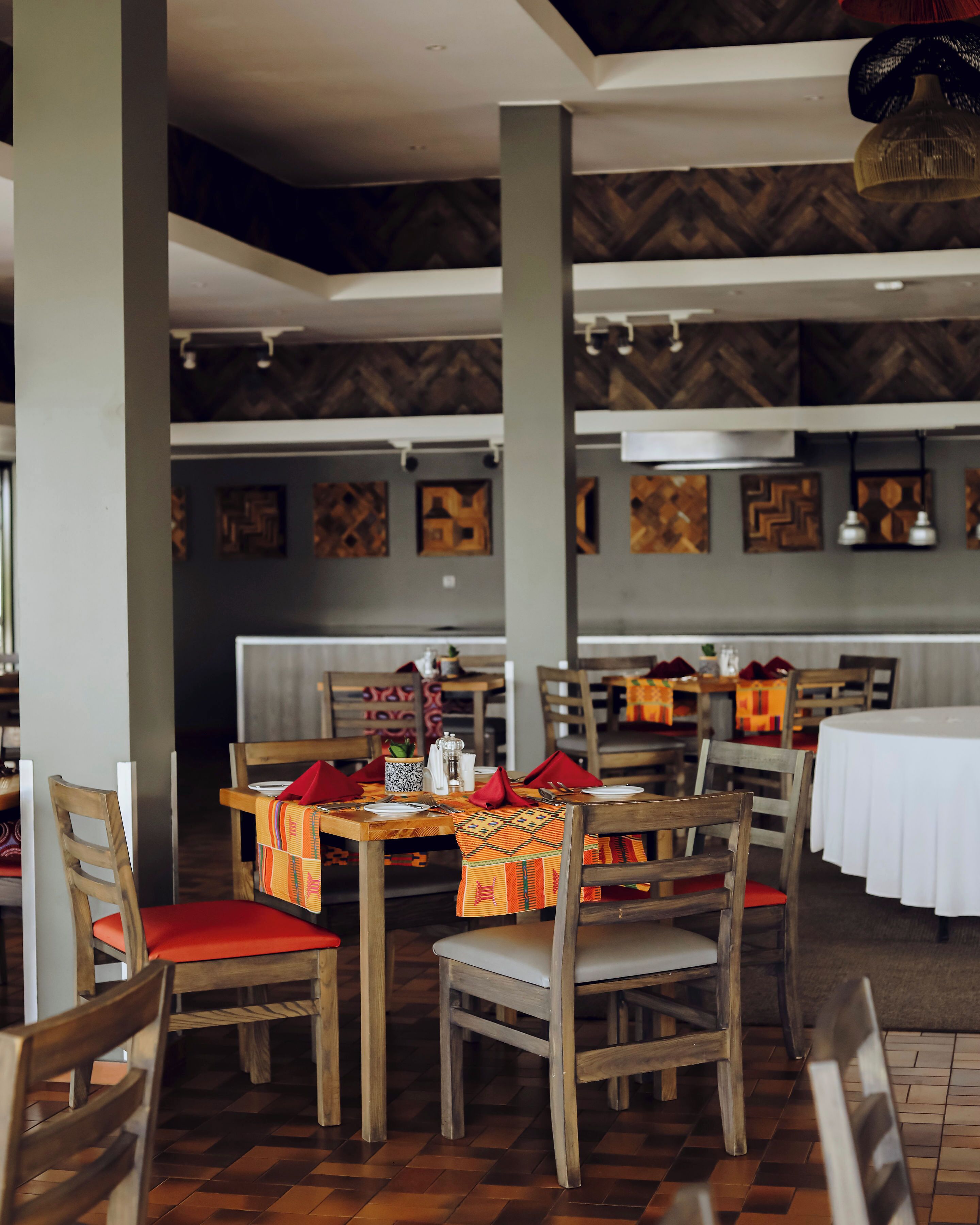 L’intérieur d’un restaurant avec des tables et des chaises en bois, une nappe à motifs et un mur orné d’un motif en chevrons.