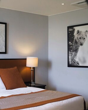 A hotel room with a bed, a nightstand with a lamp, a framed picture on the wall, and a pillow. - SALT of Akagera (Mwiri)