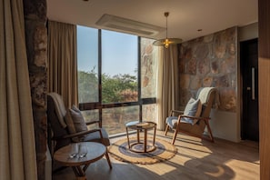 A room with a stone wall, a large window, two chairs, a small round table, and a hanging light fixture. - SALT of Akagera (Mwiri)