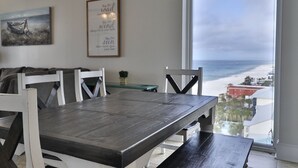 A dining area with a large table and white chairs, a view of the beach through a large window, and a framed inspirational quote on the wall. - 11th Floor 4 BR 3BA End unit in Tower 1 at the Majestic!! (Panama City Beach)