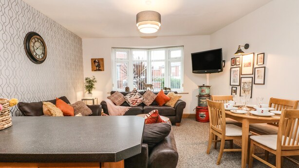 A modern living room with a sofa, a dining table set for four, a television, and a patterned wall. - Bella Vita (Southport)