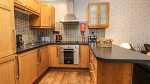 A compact kitchen with wooden cabinets, a stainless steel range, and a tiled backsplash. - Bella Vita (Southport)
