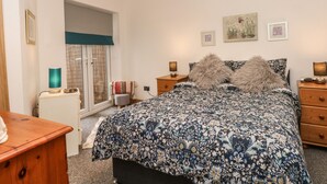 A bedroom with a floral-patterned bedspread, wooden nightstands, a desk, and a window with curtains. - Bella Vita (Southport)