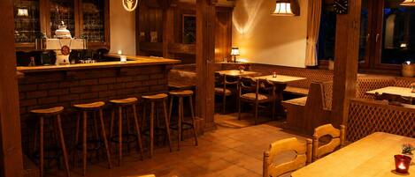 Een gezellig restaurantinterieur met houten balken, een bar en zitgedeeltes.