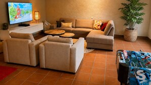 Ein Wohnzimmer mit einer Couch, zwei Sesseln, einem Couchtisch, einem Fernseher, einer Lampe und einem Kicker.