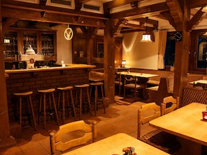 Um restaurante acolhedor com vigas de madeira, área de bar e várias mesas e cadeiras.