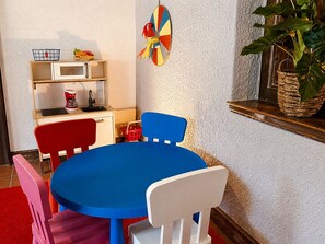 Uma sala de jantar com mesa e cadeiras azuis, micro-ondas, cafeteira e um enfeite na parede.