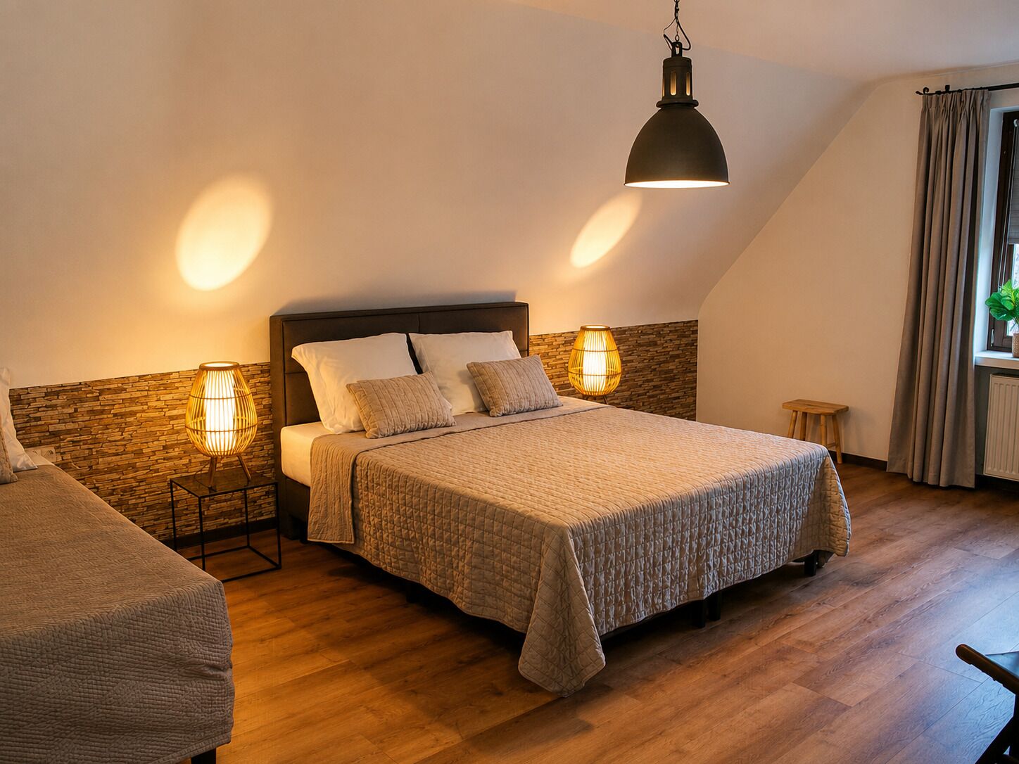 Ein Schlafzimmer mit einem Bett, zwei Nachttischlampen, einem Holzkopfteil, einem kleinen Hocker und einem Fenster mit Vorhängen.