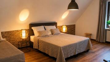 Ein Schlafzimmer mit einem Bett, zwei Nachttischlampen, einem Holzkopfteil, einem kleinen Hocker und einem Fenster mit Vorhängen.