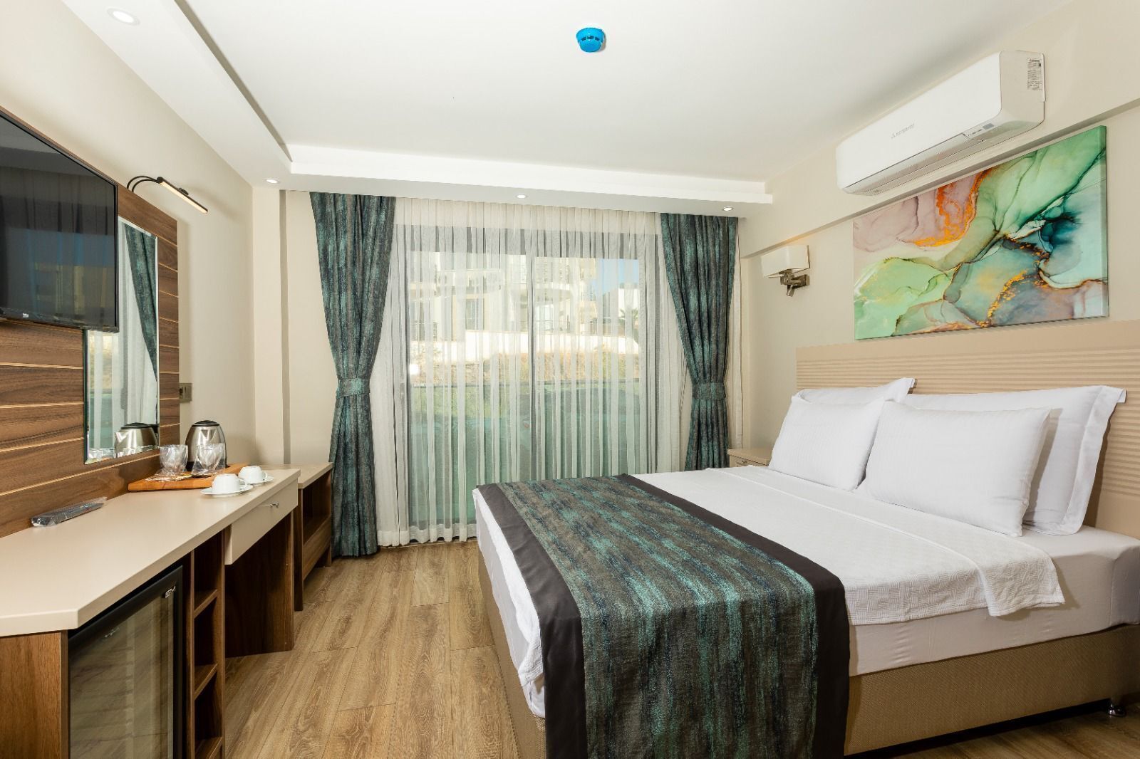 A hotel room with a bed, a desk, a television, and a window with curtains.