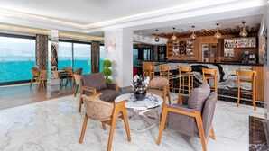 Een moderne hotel lobby met een marmeren vloer, houten meubels, een bar en uitzicht op zee.